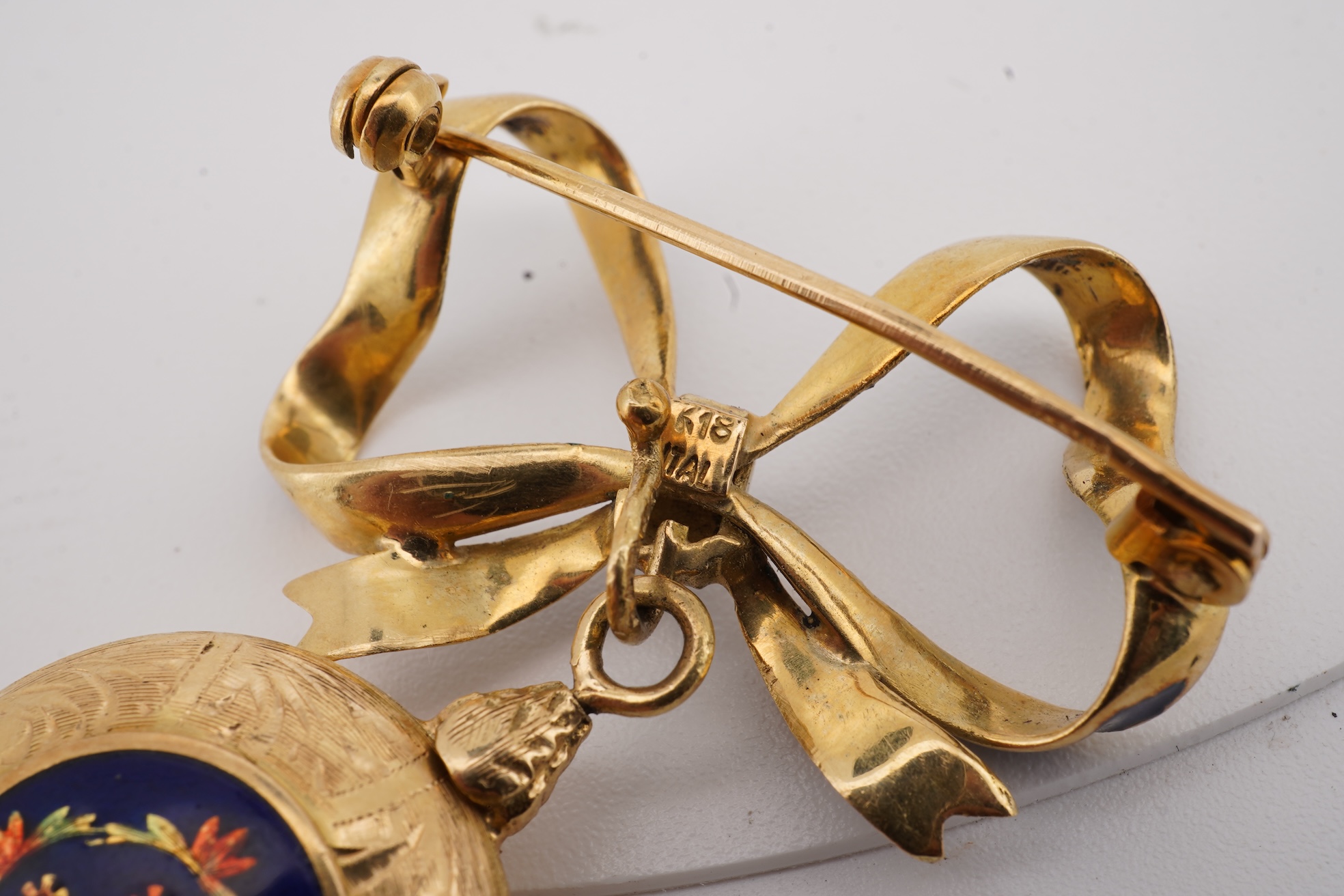 A mid 20th century Italian 18k and enamel fob watch, dial a.f., suspended from and Italian 18k and blue enamelled ribbon bow brooch, brooch width 30mm.